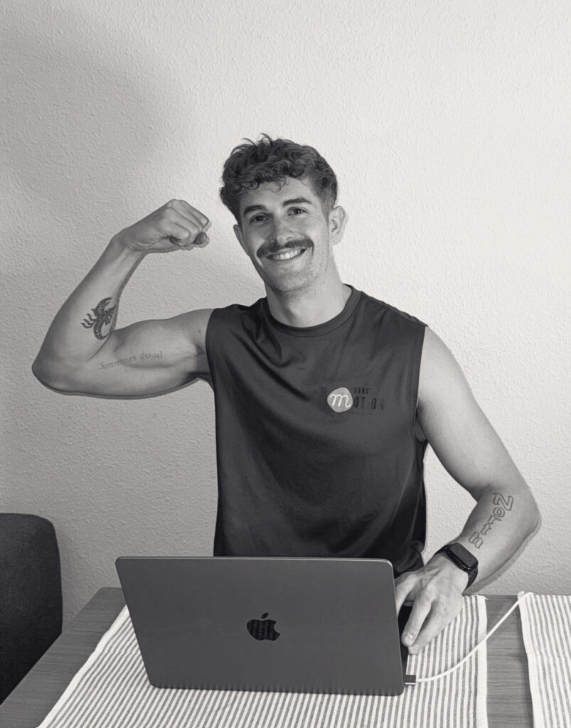 Leon Szaggars Online Coaching, Fitness Trainer: Mann in Sportkleidung sitzt am Laptop und lächelt in die Kamera. Er zeigt seinen Bizeps.
